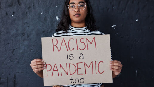 Against a royal blue background, a black banner with white text reads, "February 7 is National Black HIV/AIDS Awareness Day." Below the banner, white test reads, "NASTAD recognizes racism and the impact of structure oppression on the HIV epidemic as a public health crisis." A photograph to the right of the blue background shows a person with long brown hair, glasses, caramel colored skin and a green and white stripped shirt holding a sign that reads, "RACISM is a PANDEMIC."