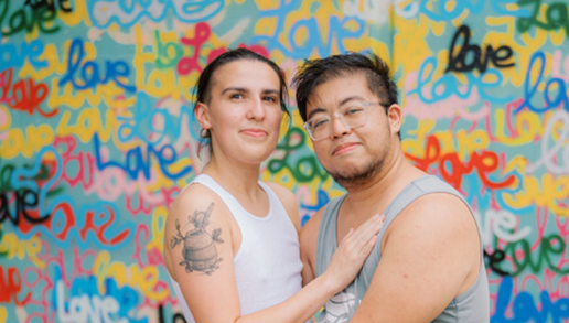 Two people embracing in front of a colorful wall
