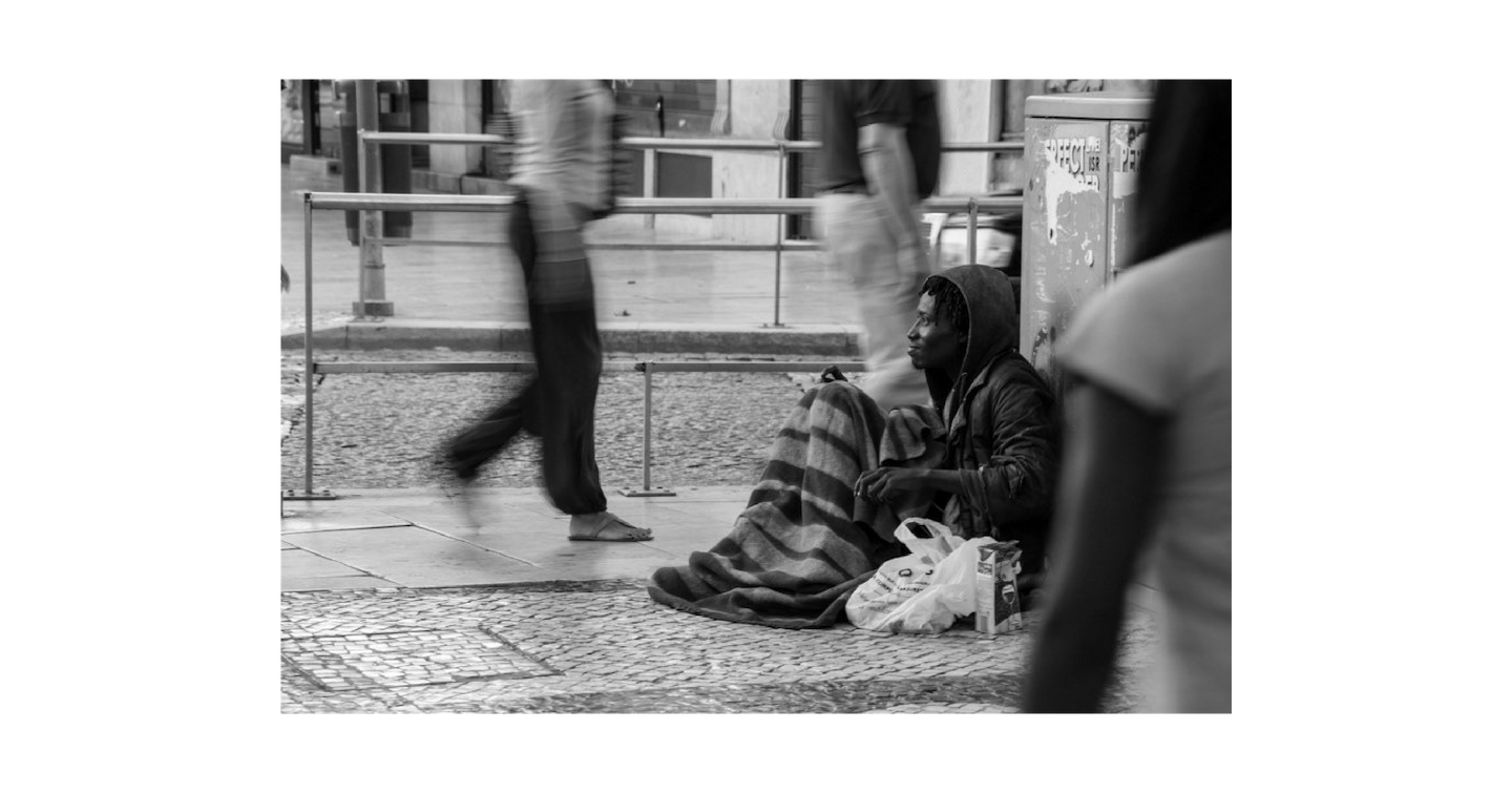 A person experiencing homelessness sitting on a sidewalk.