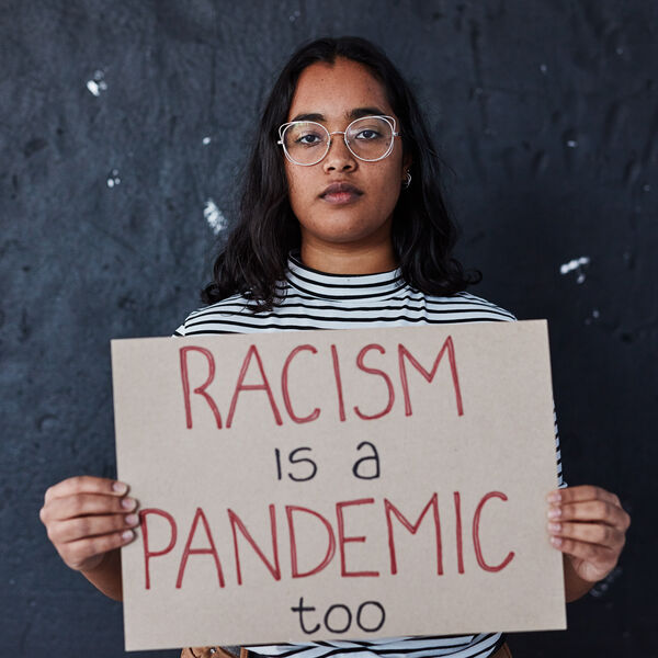 Against a royal blue background, a black banner with white text reads, "February 7 is National Black HIV/AIDS Awareness Day." Below the banner, white test reads, "NASTAD recognizes racism and the impact of structure oppression on the HIV epidemic as a public health crisis." A photograph to the right of the blue background shows a person with long brown hair, glasses, caramel colored skin and a green and white stripped shirt holding a sign that reads, "RACISM is a PANDEMIC."