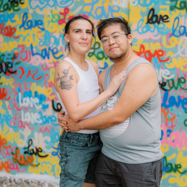 Two people embracing in front of a colorful wall